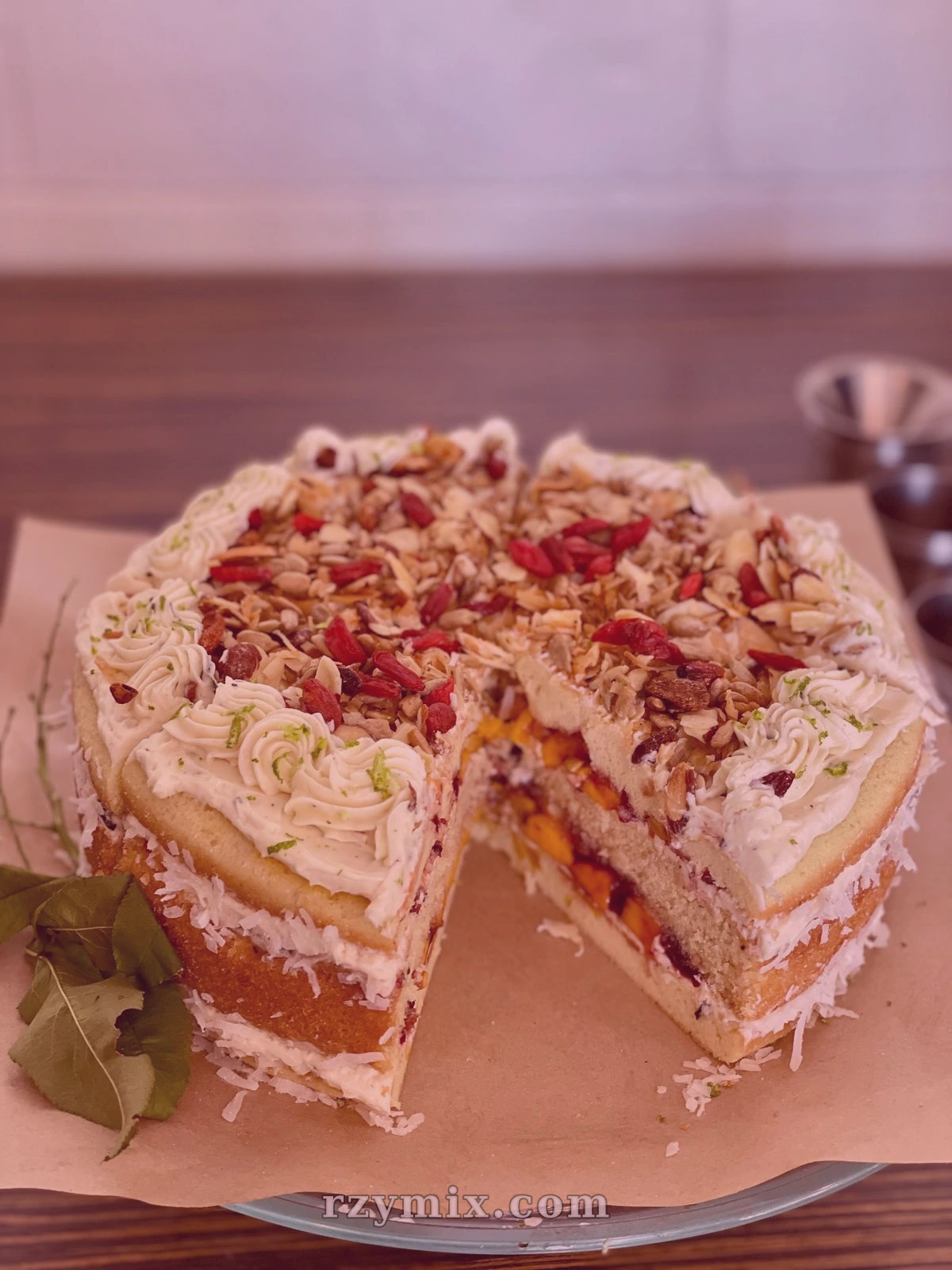 mango coconut cake filled with blackberry raspberry jam, decorated with basil buttercream, and topped with coconut, toasted almonds, goji berries, and sunflower seeds
